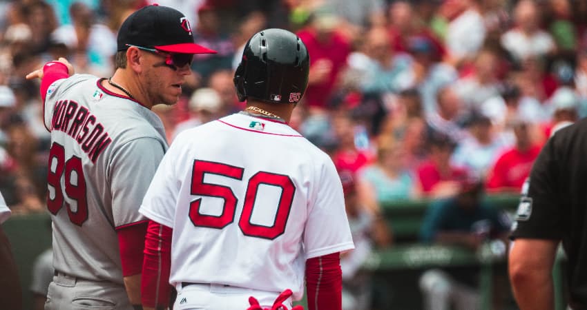 Two baseball player talk on the field, fans filling the seats of Fenway Park in Boston