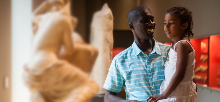 a father and his daughter smile and look at sculptures in an art museum