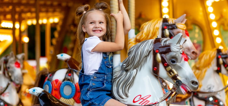 a child smiles while riding a horse on a carousel