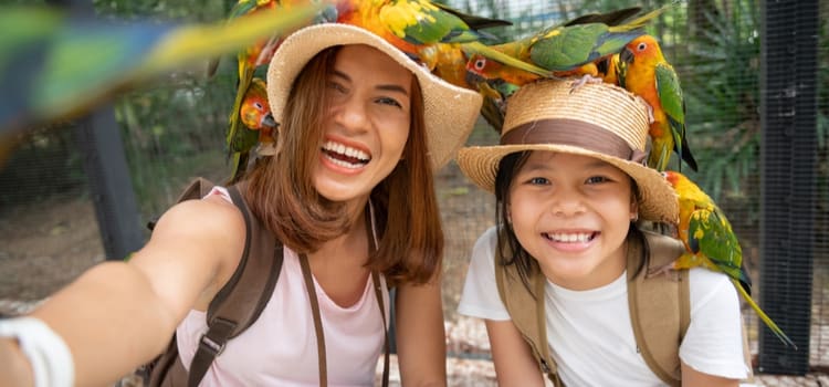 a parent and child in hats smile for pictures while surrounded by birds