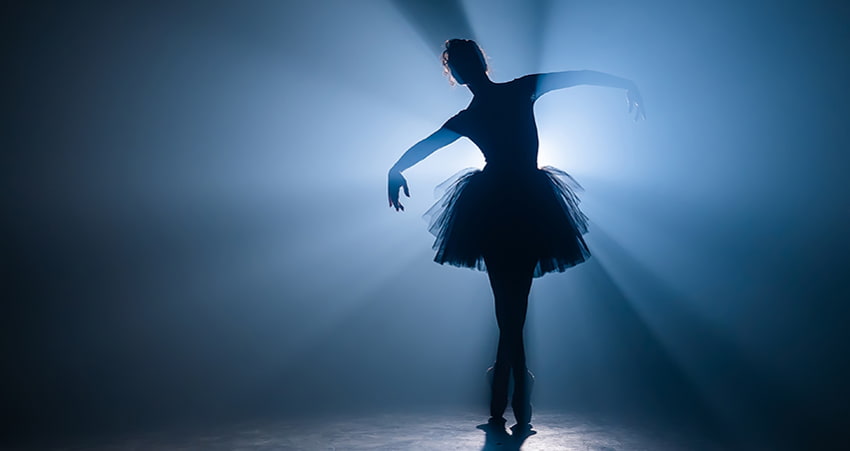 A ballet dancer poses on a dimly lit stage